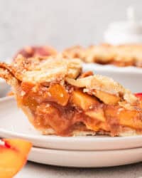 A slice of peach pie on a white plate, with the rest of the pie in the background.