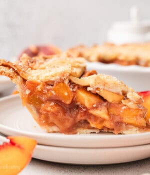 A slice of peach pie on a white plate, with the rest of the pie in the background.