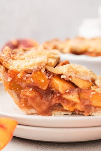 A slice of peach pie on a white plate, with the rest of the pie in the background.