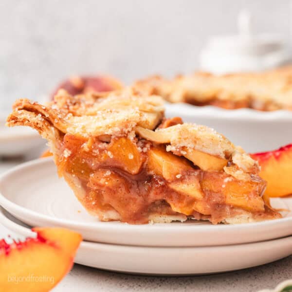 A slice of peach pie on a white plate, with the rest of the pie in the background.