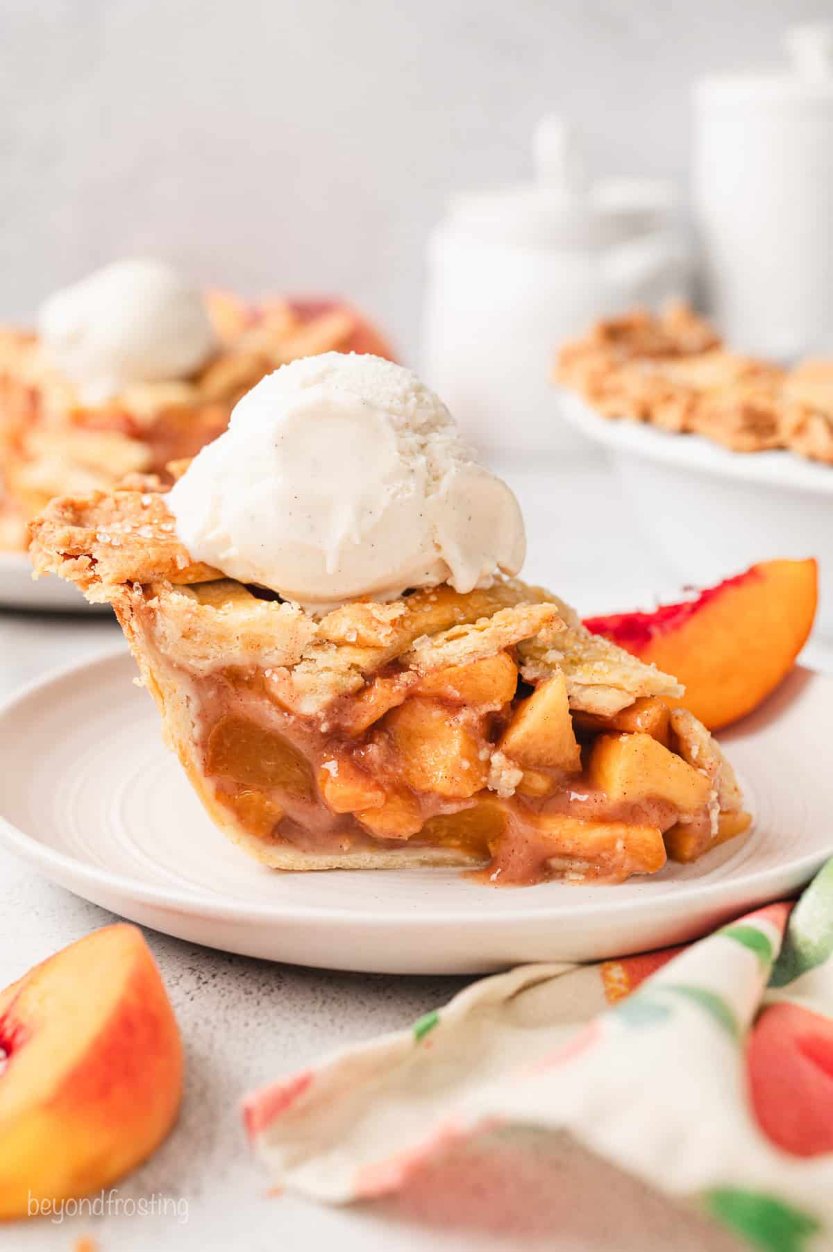 A slice of peach pie topped with a scoop of ice cream on a white plate.