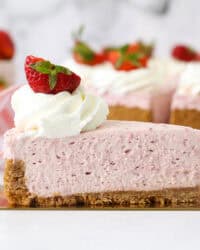 A slice of no-bake strawberry cheesecake on a cake server, with the rest of the cheesecake in the background.