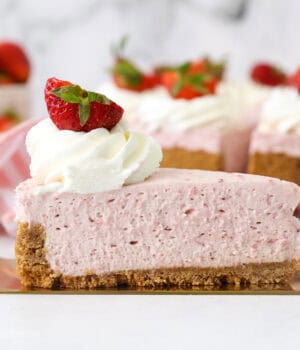 A slice of no-bake strawberry cheesecake on a cake server, with the rest of the cheesecake in the background.