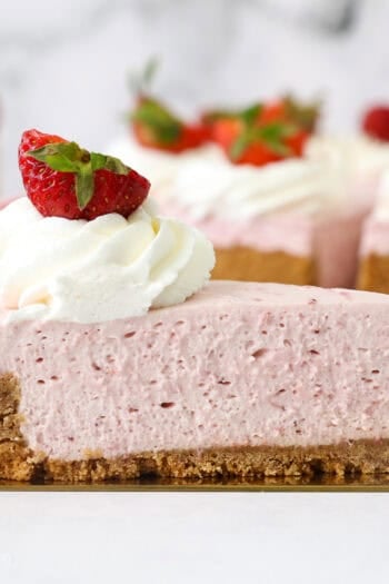 A slice of no-bake strawberry cheesecake on a cake server, with the rest of the cheesecake in the background.