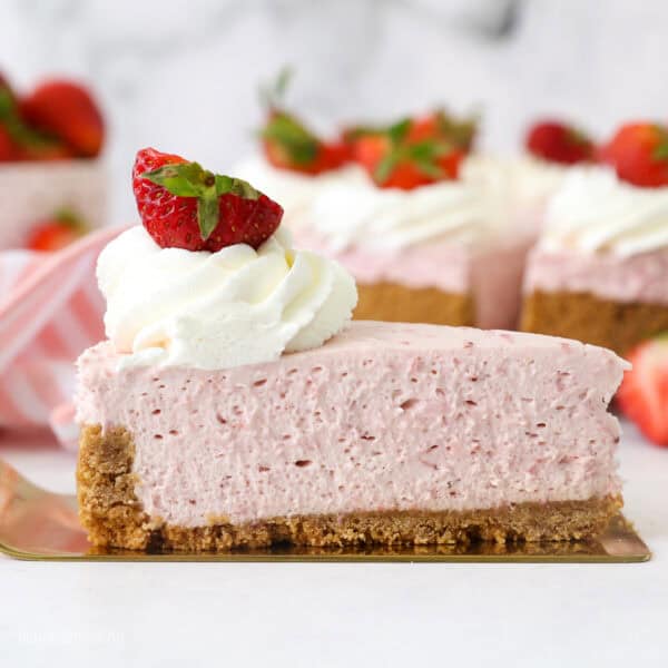 A slice of no-bake strawberry cheesecake on a cake server, with the rest of the cheesecake in the background.