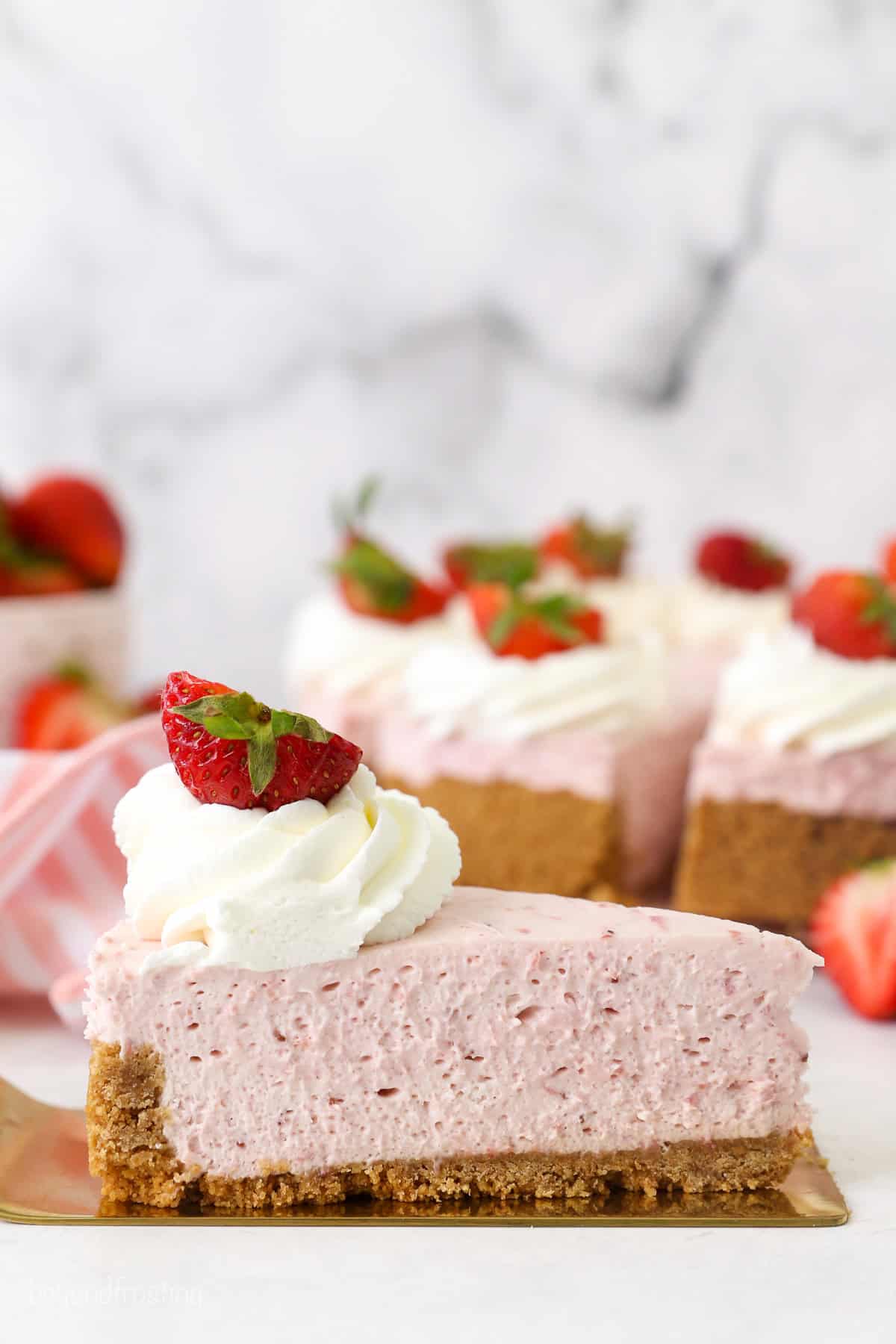 A slice of no-bake strawberry cheesecake on a cake server, with the rest of the cheesecake in the background.