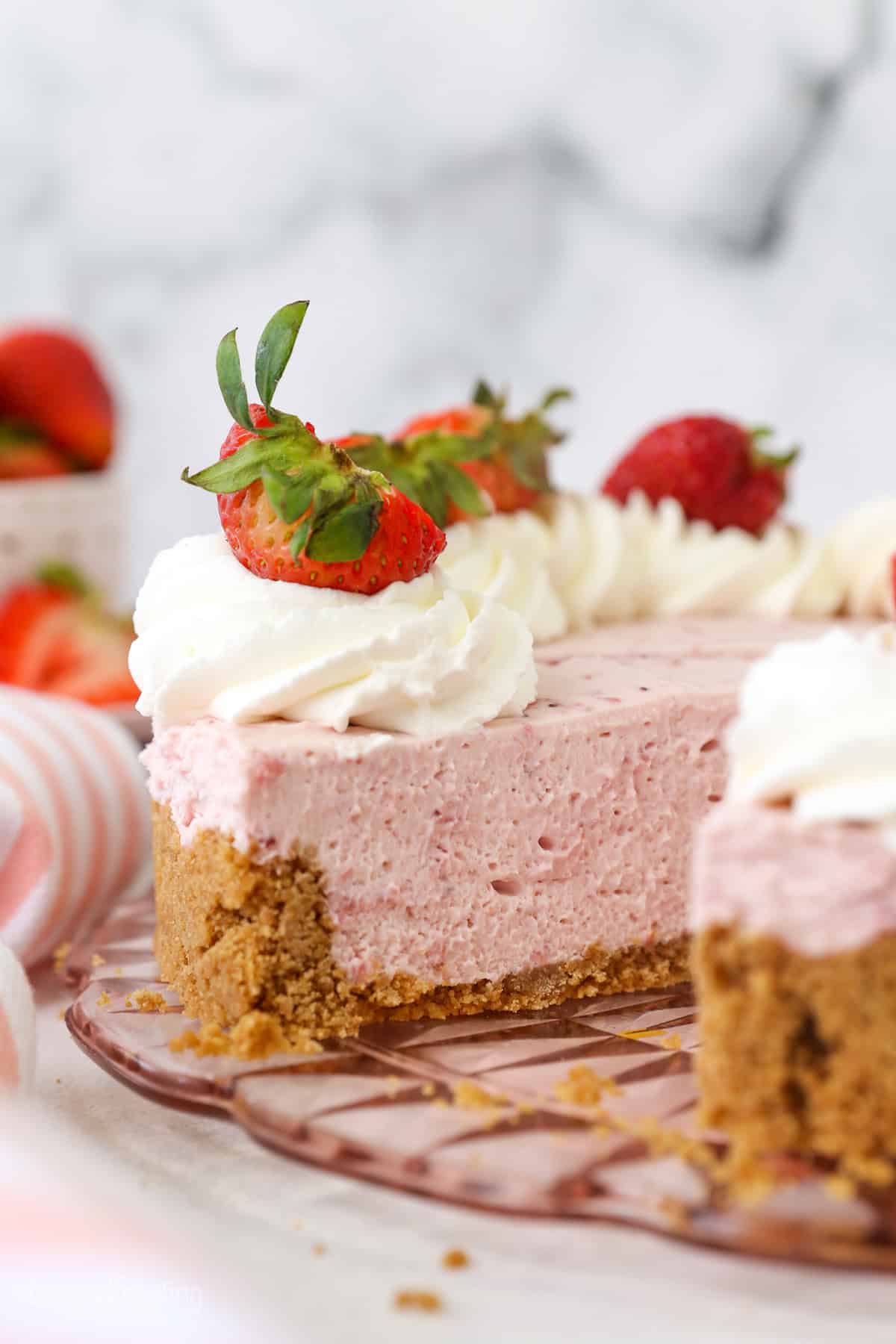 No-bake strawberry cheesecake topped with swirls of whipped cream and fresh strawberries, with a large slice missing.