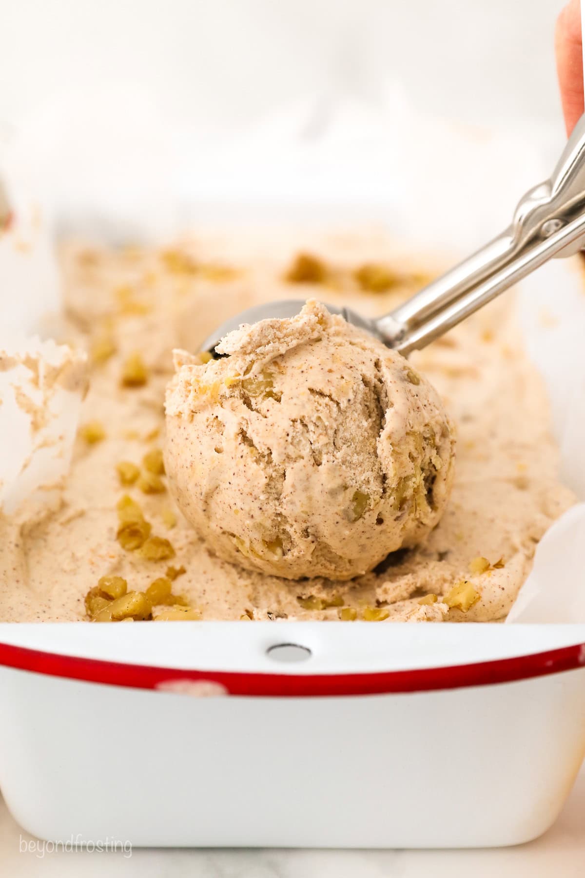 A white loaf pan with a ice cream scoop full of peach ice cream