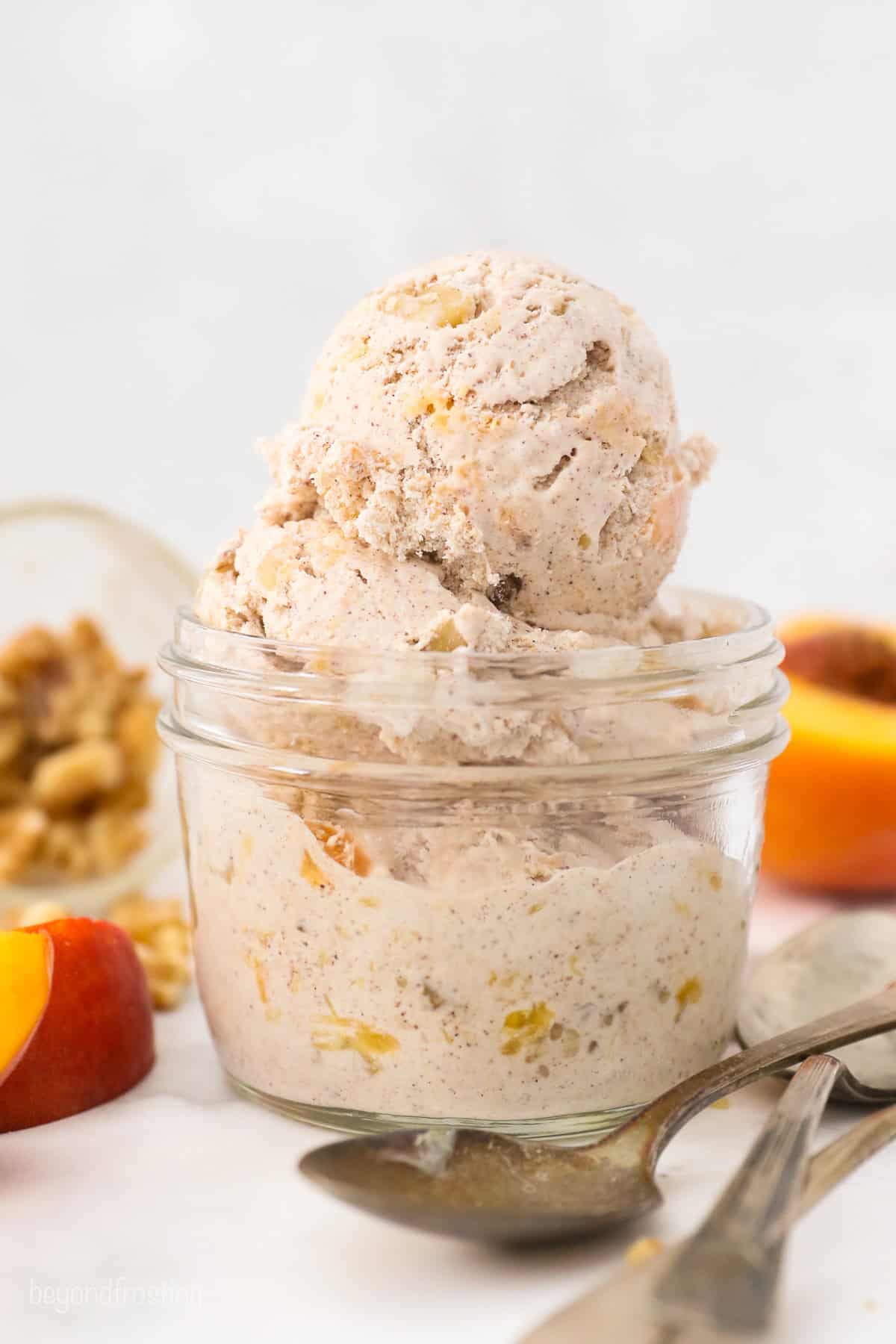 A small glass mason jar with scoops of peach ice cream and two spoons next to it