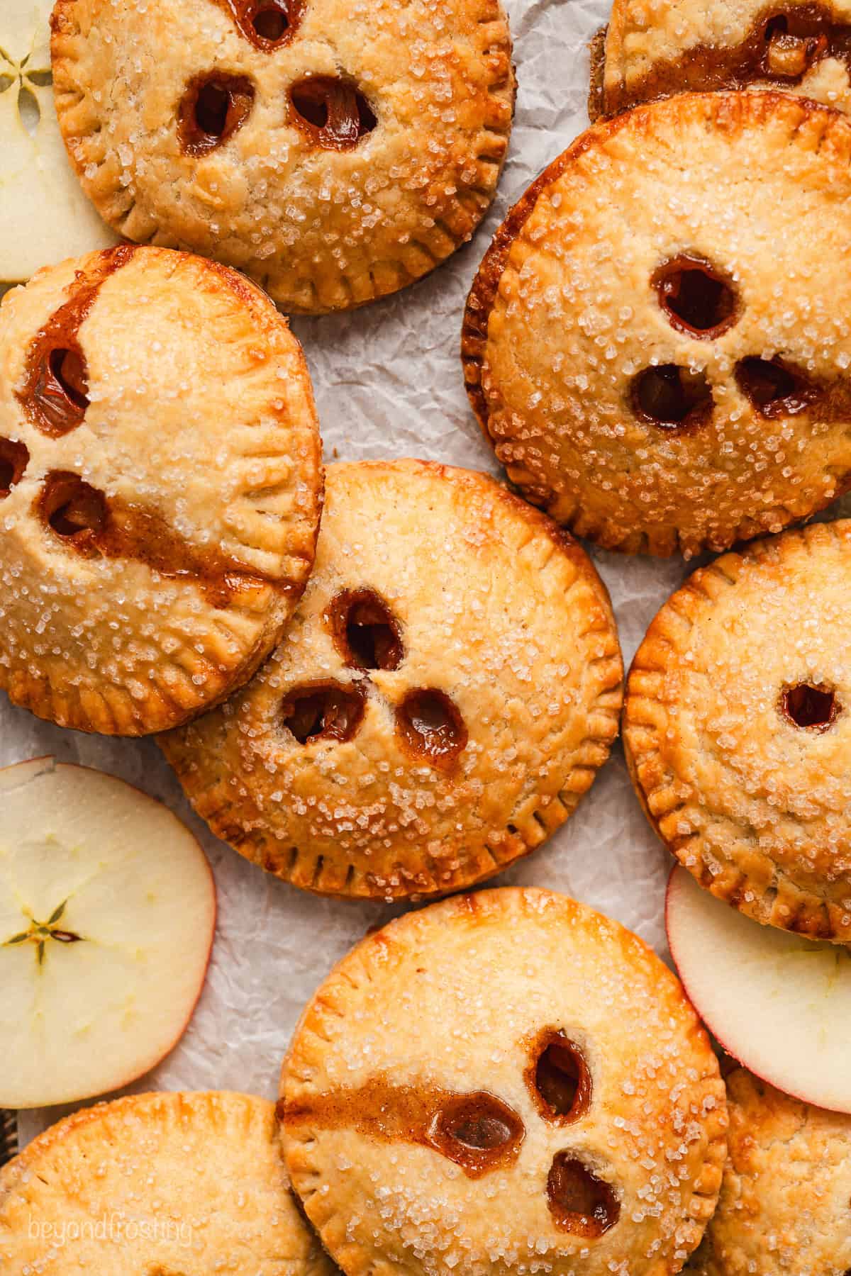 Overhead view of baked apple hand pies scattered among fresh apple slices.