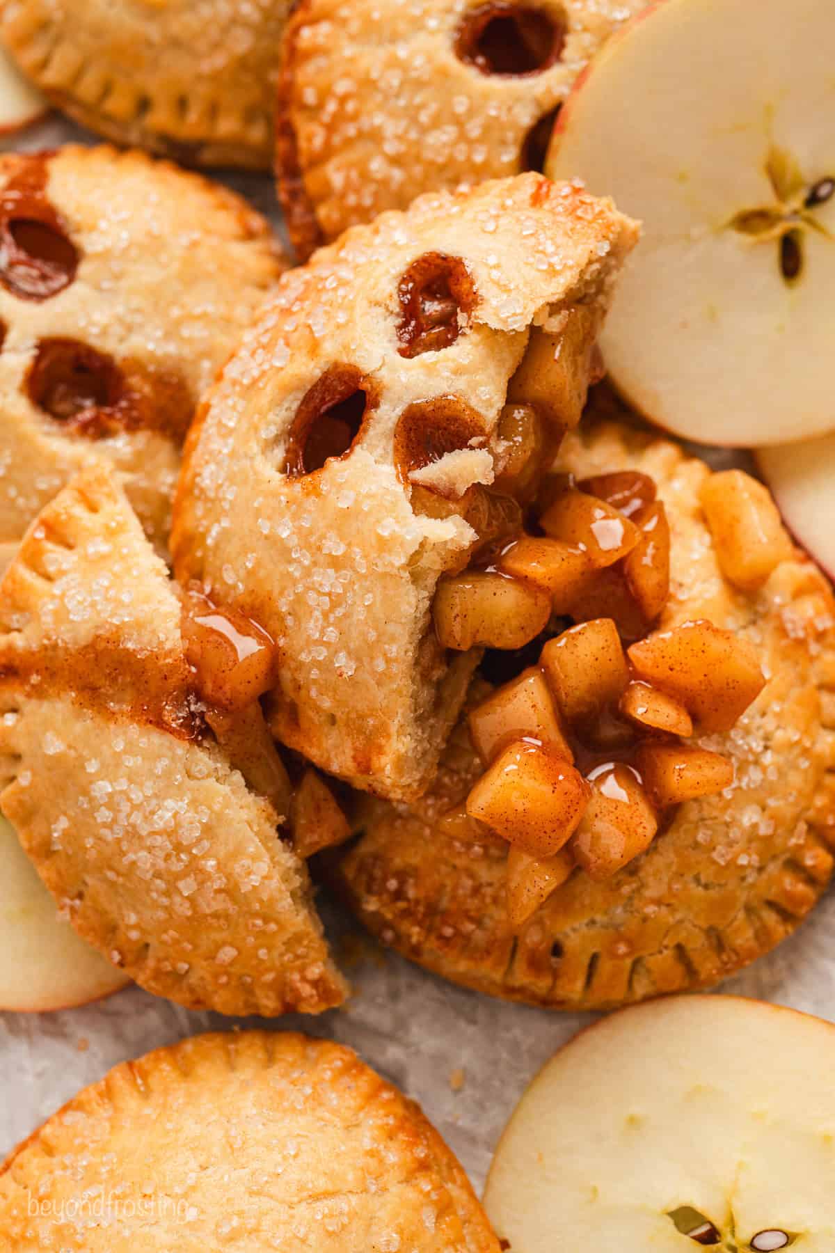 Close up overhead view of one half of an apple hand pie spilling apple filling over a pile of hand pies below.