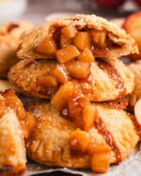 Close up side view of one half of an apple hand pie spilling apple filling over a pile of hand pies below.