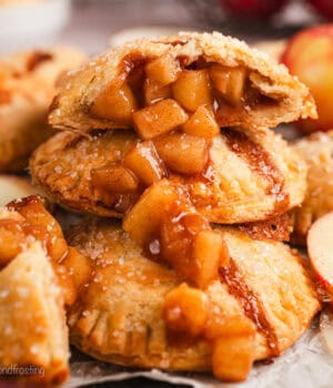 Close up side view of one half of an apple hand pie spilling apple filling over a pile of hand pies below.