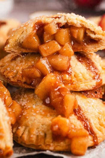 Close up side view of one half of an apple hand pie spilling apple filling over a pile of hand pies below.