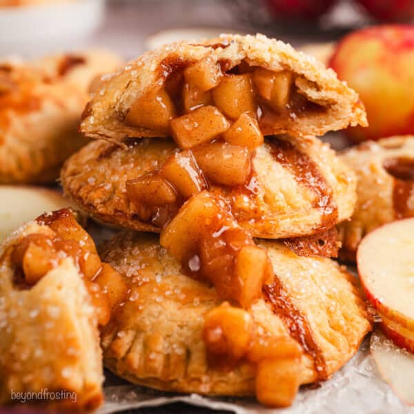 Close up side view of one half of an apple hand pie spilling apple filling over a pile of hand pies below.