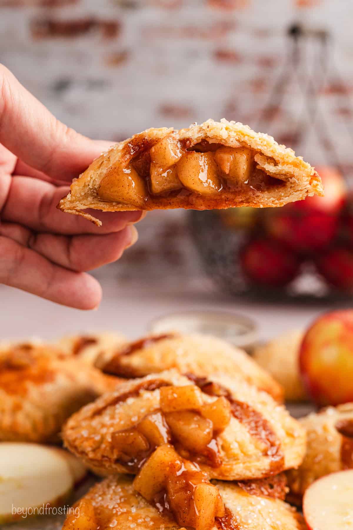 A hand lifting up one half of an apple hand pie, with the other half stacked on more hand pies below.