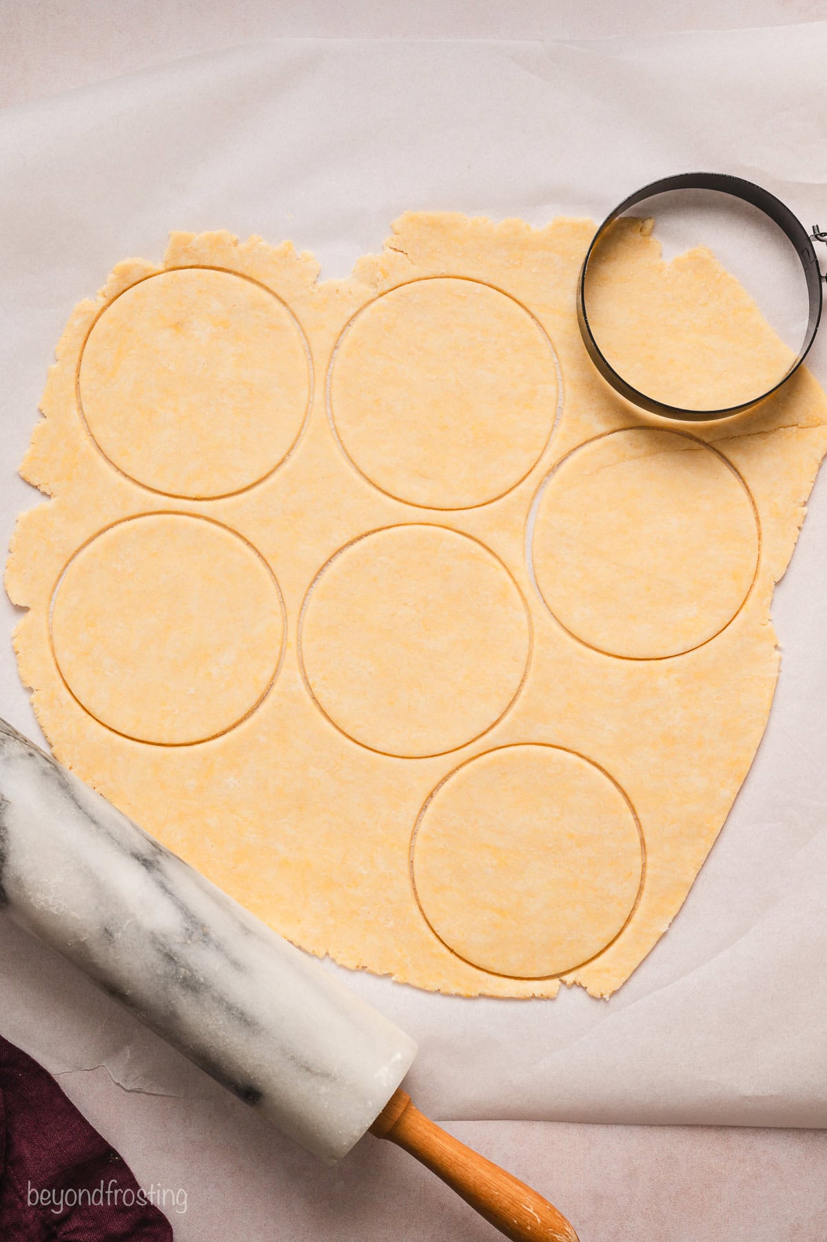 A metal biscuit cutter resting on rolled out pie dough on parchment paper, with circles pressed into the dough.