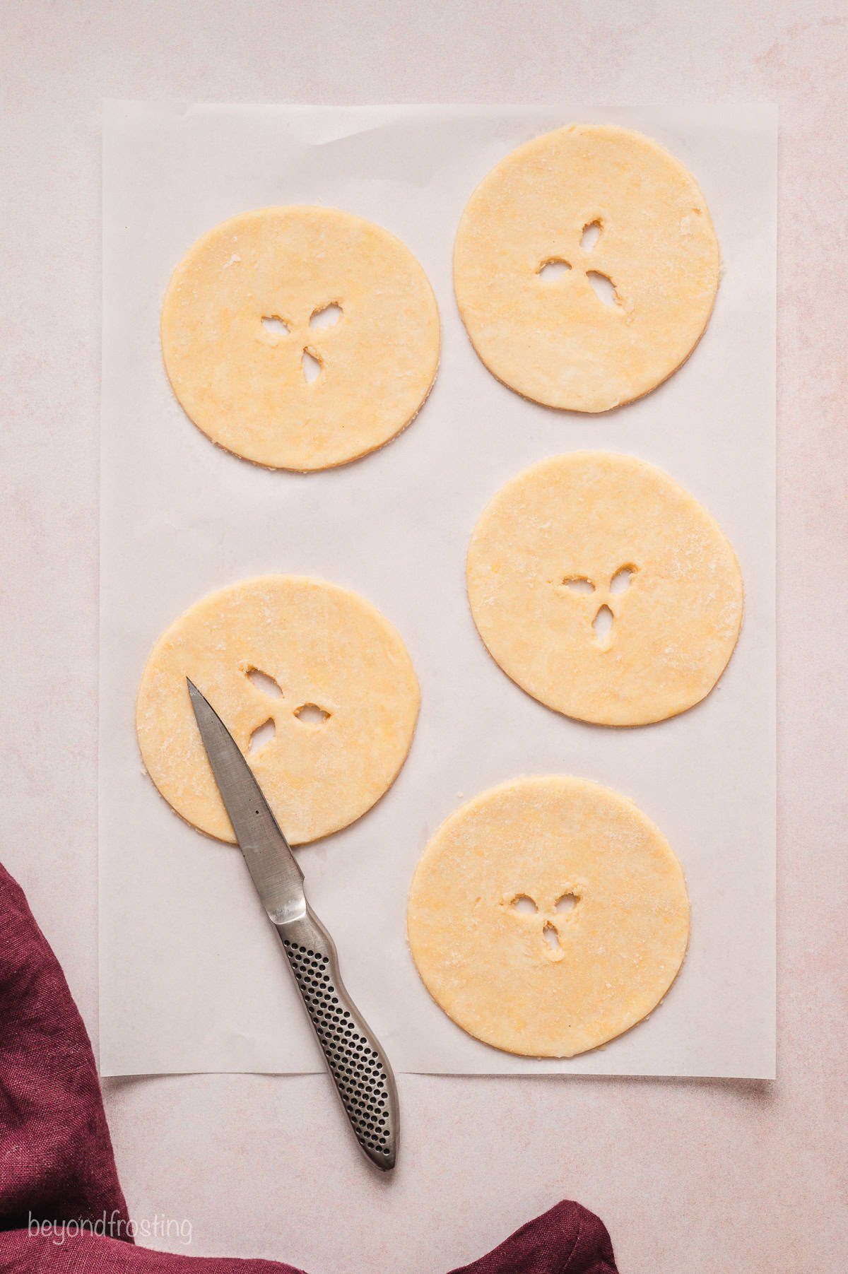 A sharp knife laying next to three round pie crusts with small vent holes cut in the center.