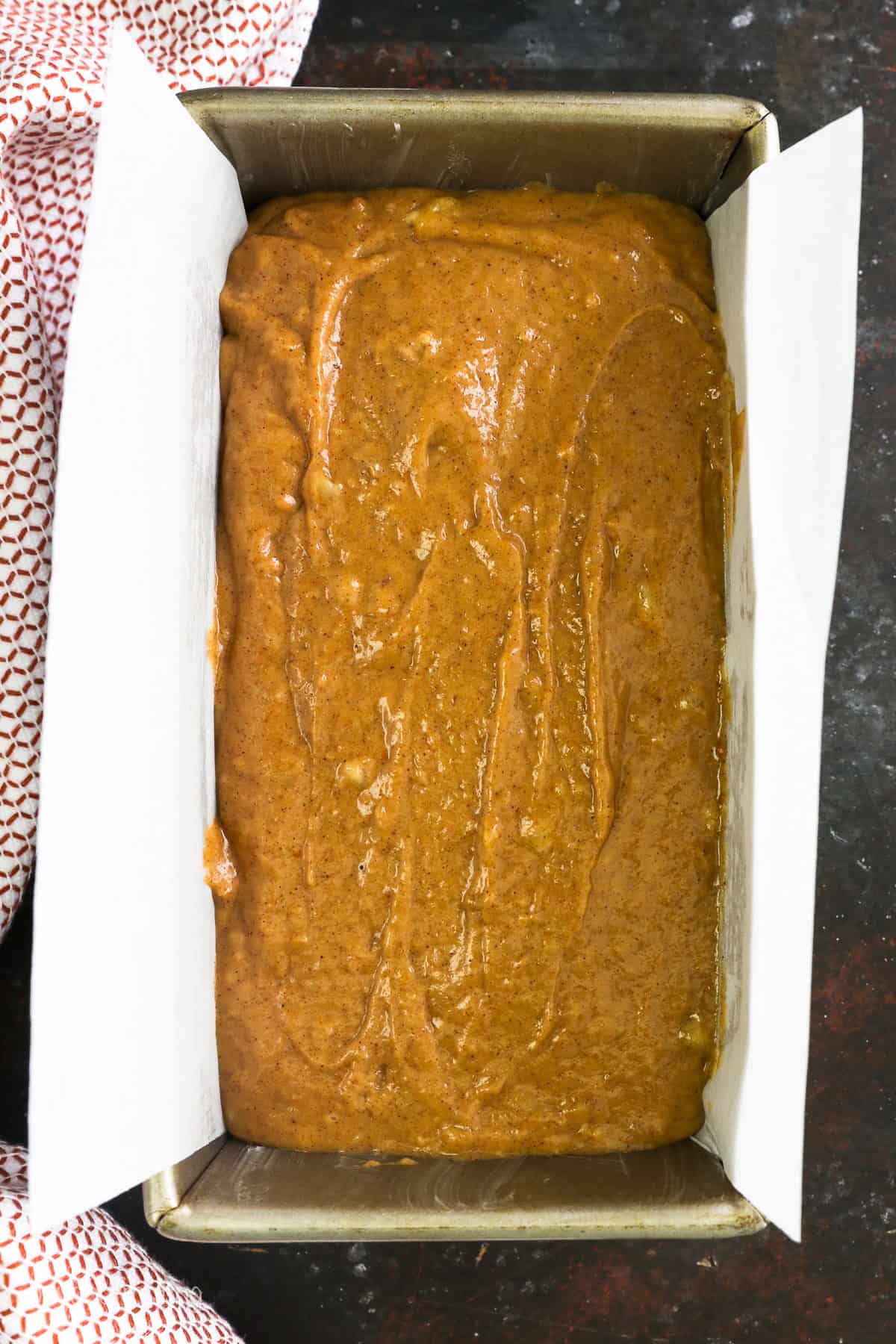 Overhead view of pumpkin banana bread batter in a lined loaf pan.