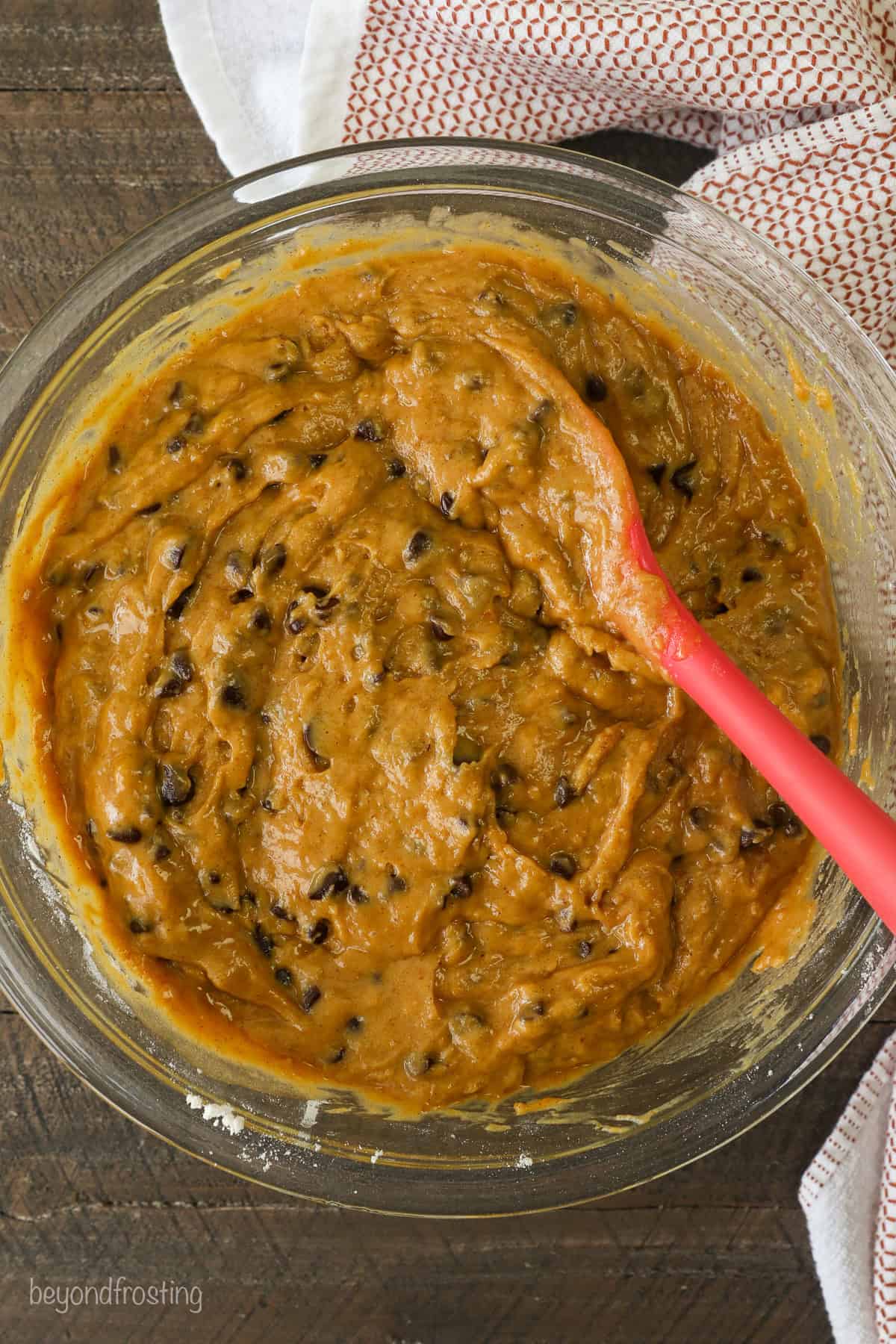 Pumpkin chocolate chip muffin batter in a glass bowl with a red rubber spoon.