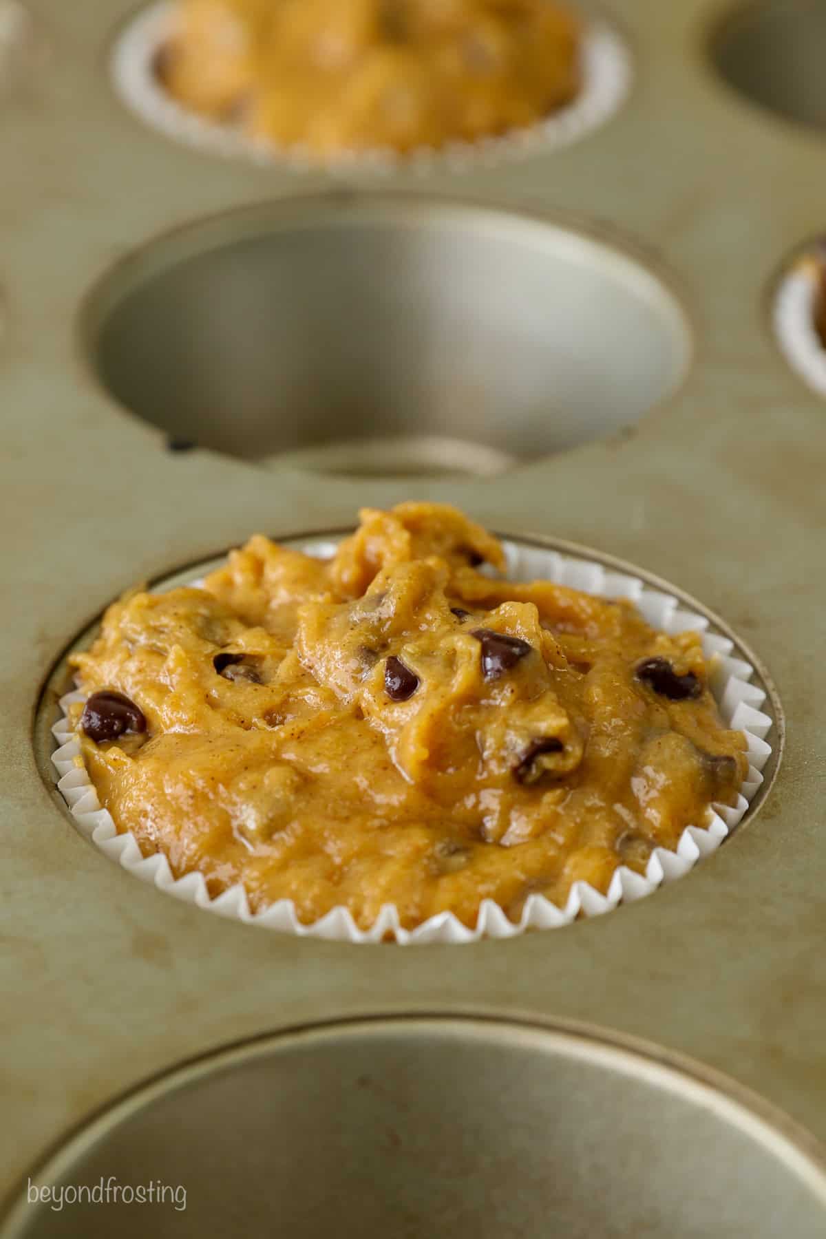 Close up of pumpkin chocolate chip muffin batter in alternating wells of a muffin tin.