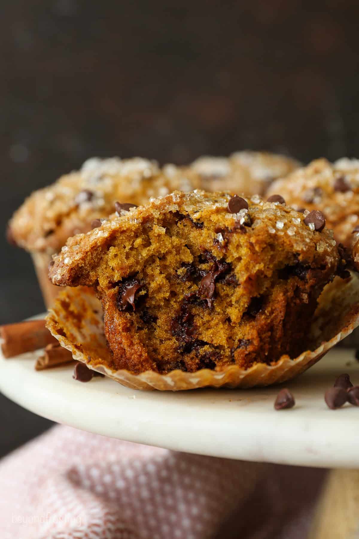 Close up of a pumpkin chocolate chip muffin with a bite missing, with more muffins in the background.