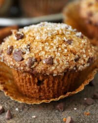 Close up of a pumpkin chocolate chip muffin topped with sparkling sugar, with more muffins in the background.