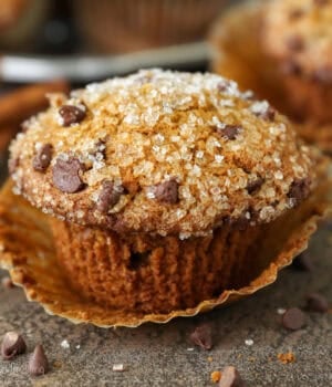 Close up of a pumpkin chocolate chip muffin topped with sparkling sugar, with more muffins in the background.