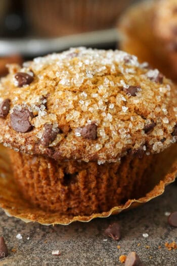 Close up of a pumpkin chocolate chip muffin topped with sparkling sugar, with more muffins in the background.