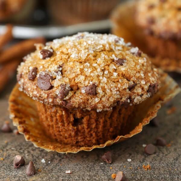 Close up of a pumpkin chocolate chip muffin topped with sparkling sugar, with more muffins in the background.