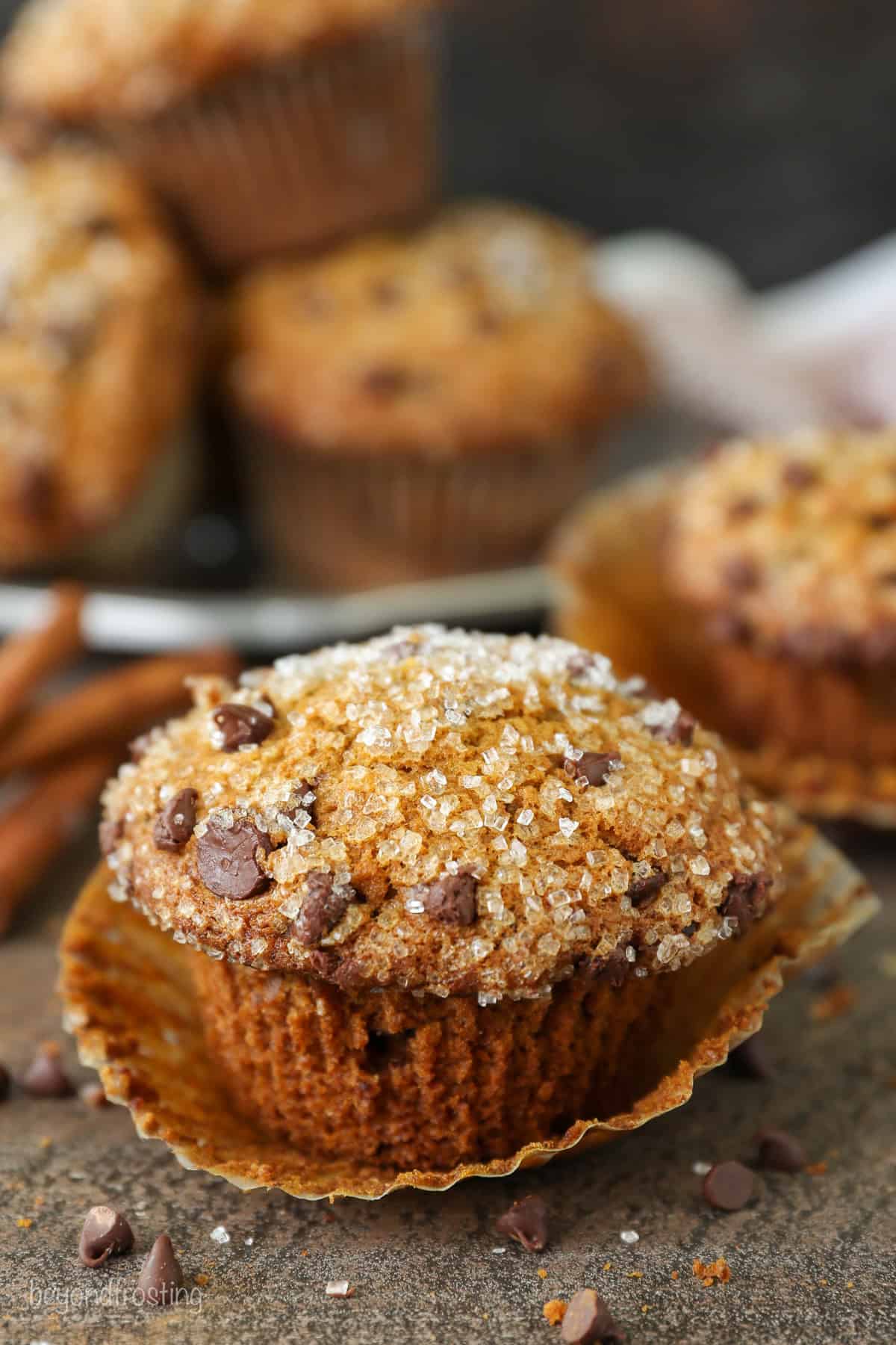 Close up of a pumpkin chocolate chip muffin topped with sparkling sugar, with more muffins in the background.