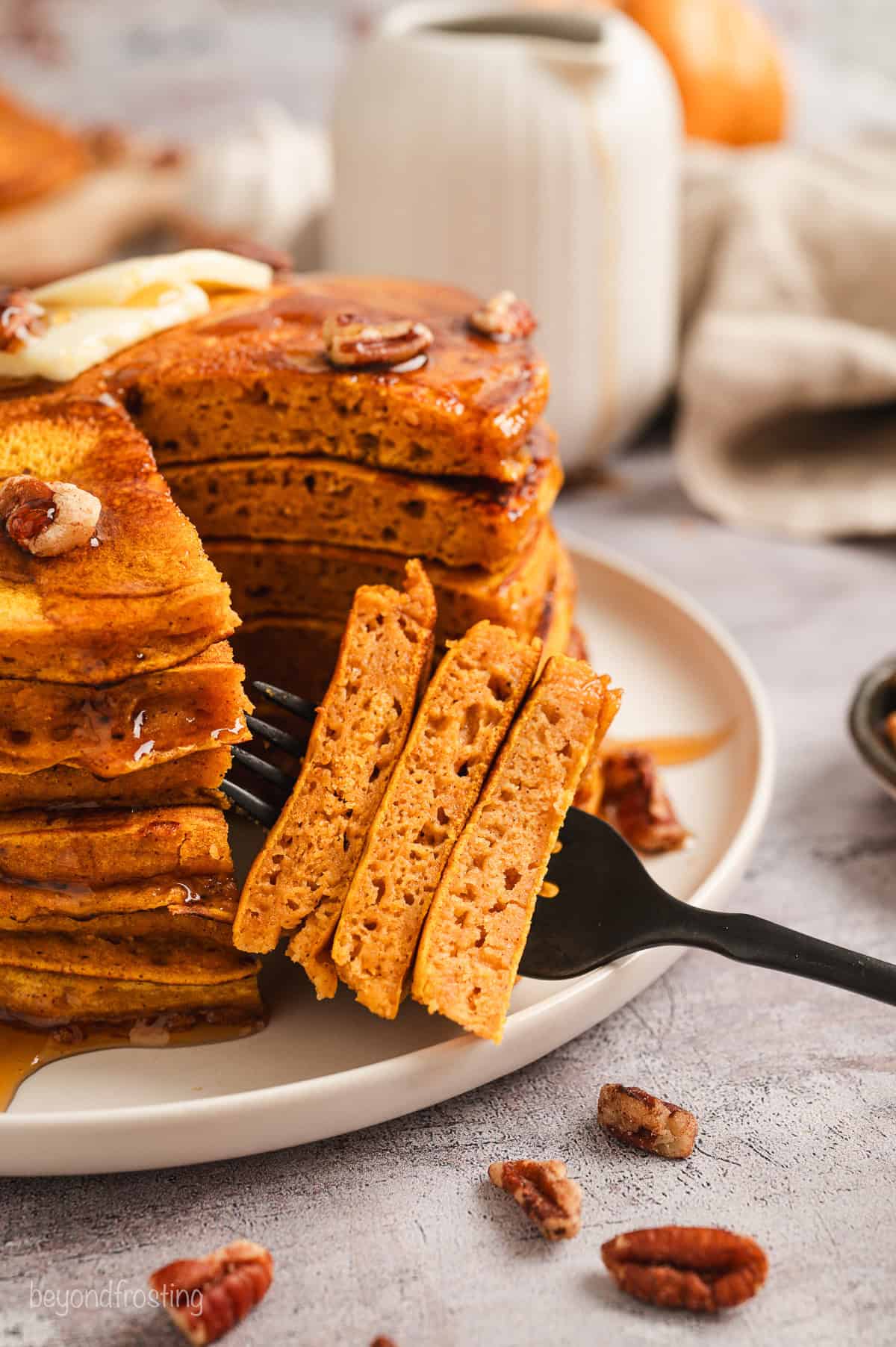 A forkful of pumpkin pancakes cut from a stack of pancakes on a plate.