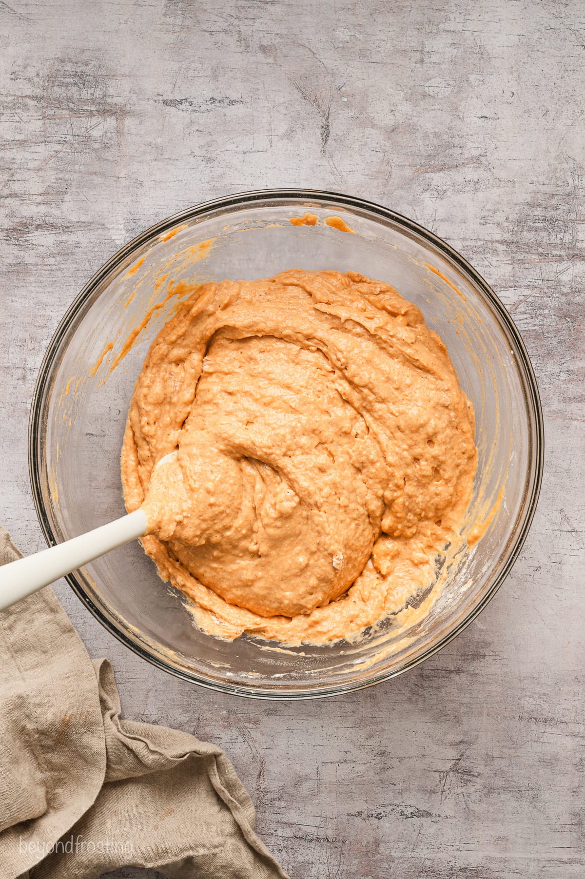 Pumpkin pancake batter in a glass bowl with a wooden spoon.