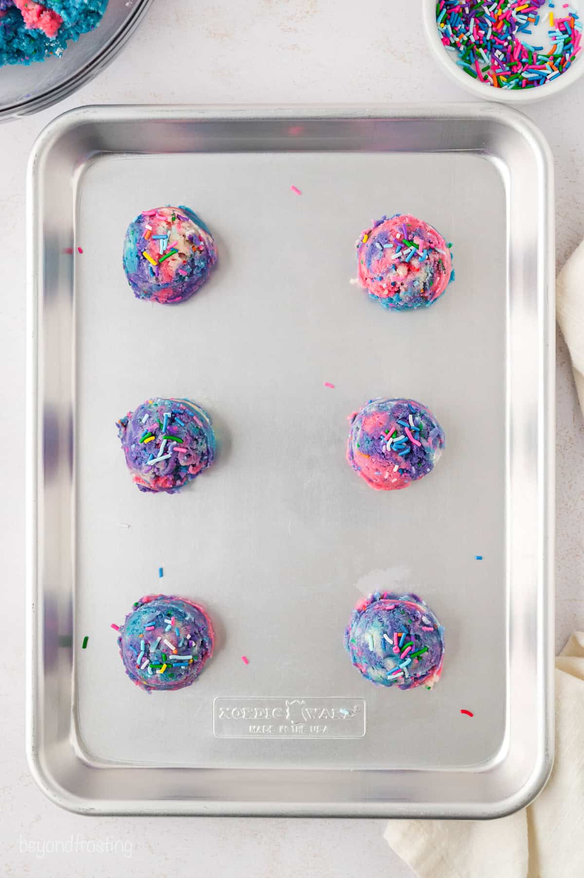 Balls of unicorn sugar cookie dough arranged on a metal baking tray.