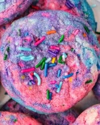 A close up of a tye dye cookie with pink, blue and purple with sprinkles made to look like Unicorn Poop