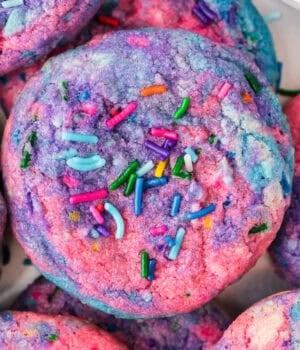 A close up of a tye dye cookie with pink, blue and purple with sprinkles made to look like Unicorn Poop