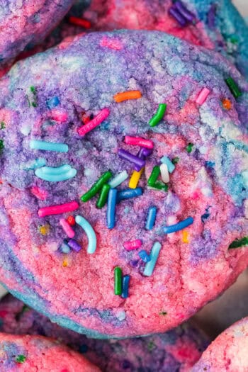 A close up of a tye dye cookie with pink, blue and purple with sprinkles made to look like Unicorn Poop