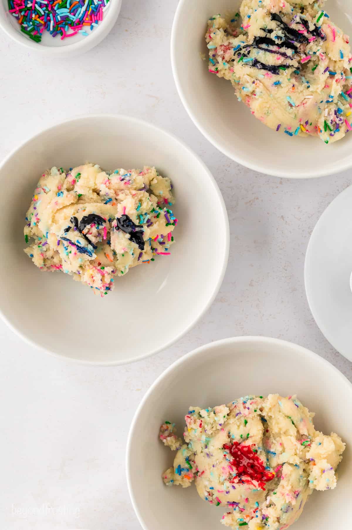 Sprinkle cookie dough portioned into three separate white bowls.