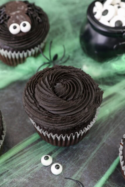 A chocolate cupcake with a black buttercream swirl and candy eyeballs on the side