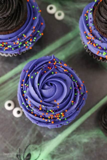 A purple rose on top of a cupcake with halloween sprinkles