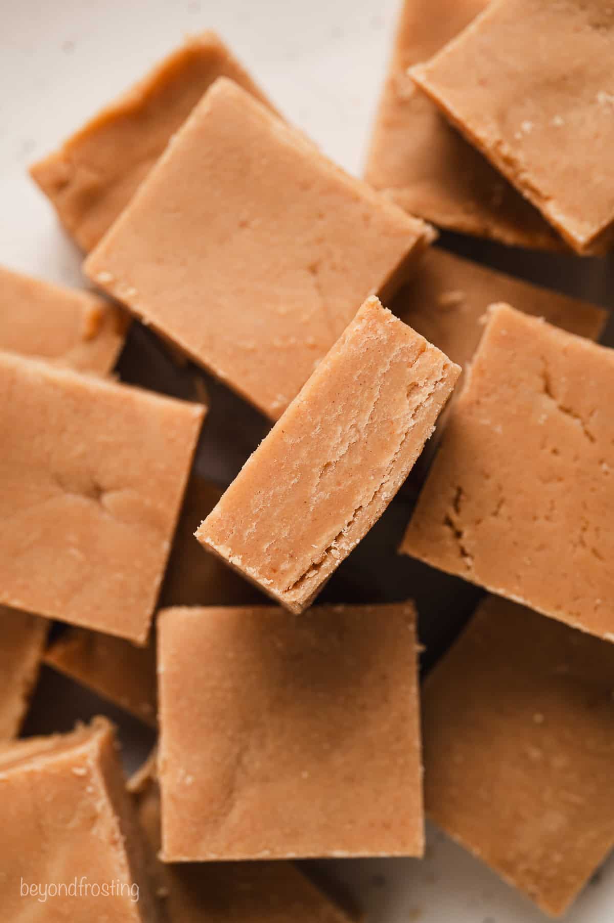 Overhead close up view of assorted peanut butter fudge squares stacked on a white countertop.