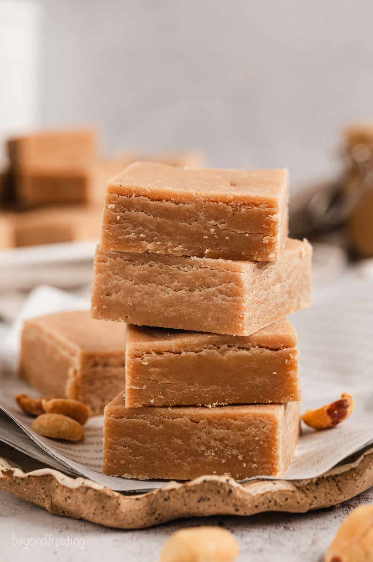 Classic peanut butter fudge squares stacked on a piece of parchment paper.