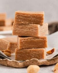 Classic peanut butter fudge squares stacked on a piece of parchment paper.