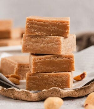 Classic peanut butter fudge squares stacked on a piece of parchment paper.