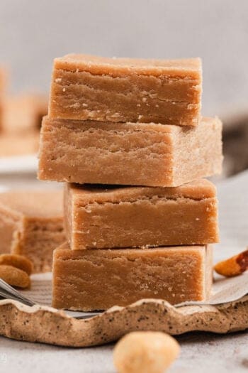 Classic peanut butter fudge squares stacked on a piece of parchment paper.