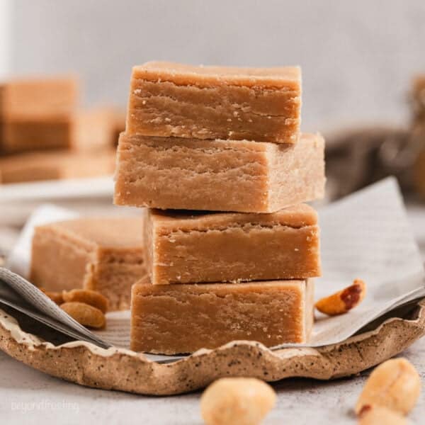 Classic peanut butter fudge squares stacked on a piece of parchment paper.