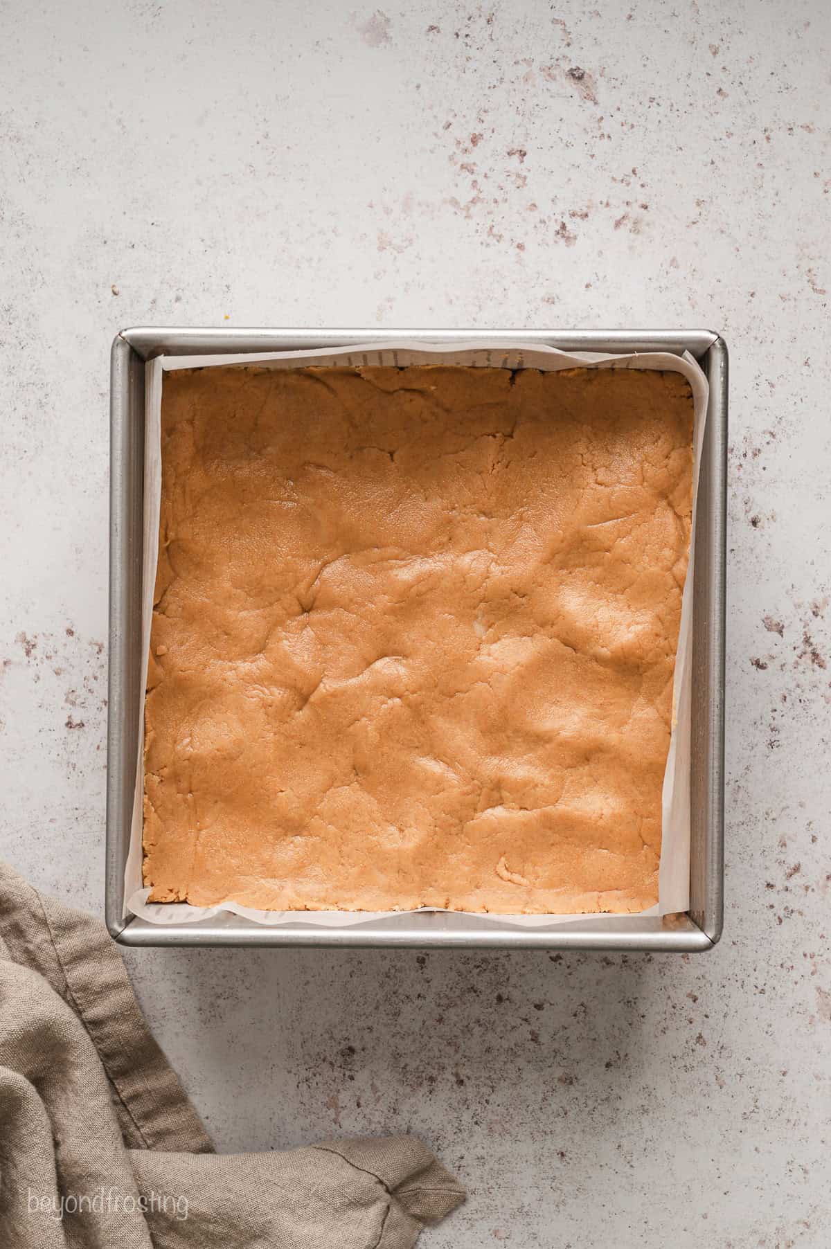 Peanut butter fudge pressed into the bottom of a lined square baking pan.