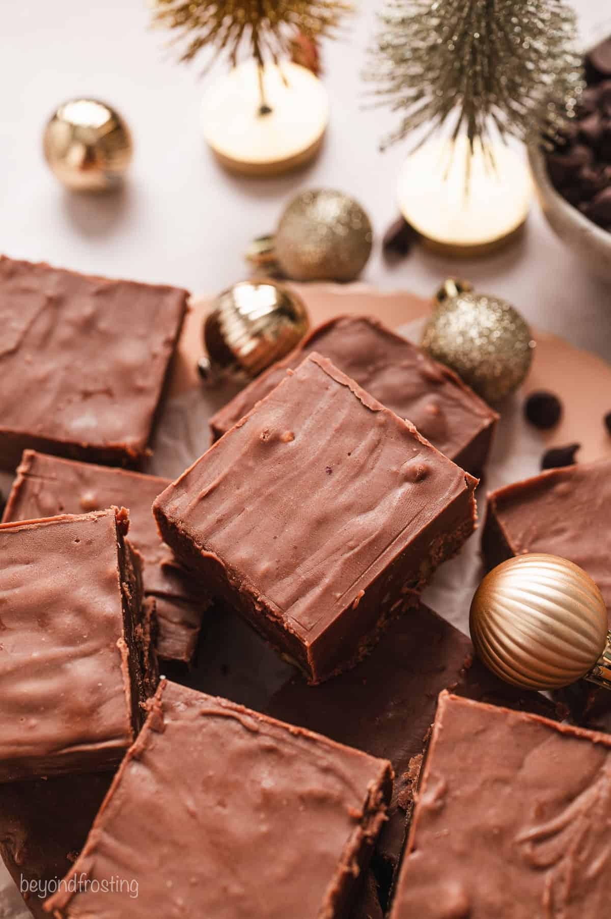 Overhead view of fantasy fudge stacked on a wooden platter next to Christmas ornaments on a countertop.