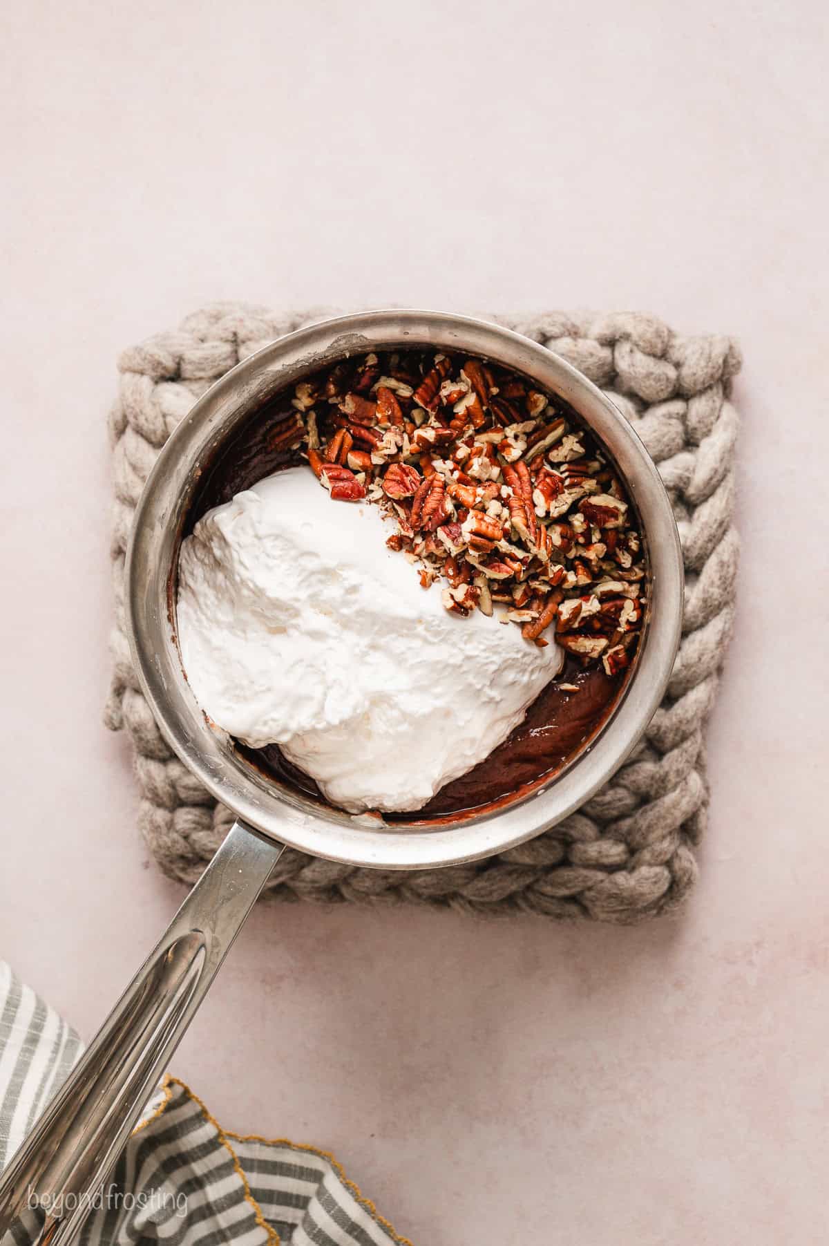 Marshmallow creme and chopped pecans added to the fudge mixture in a saucepan.