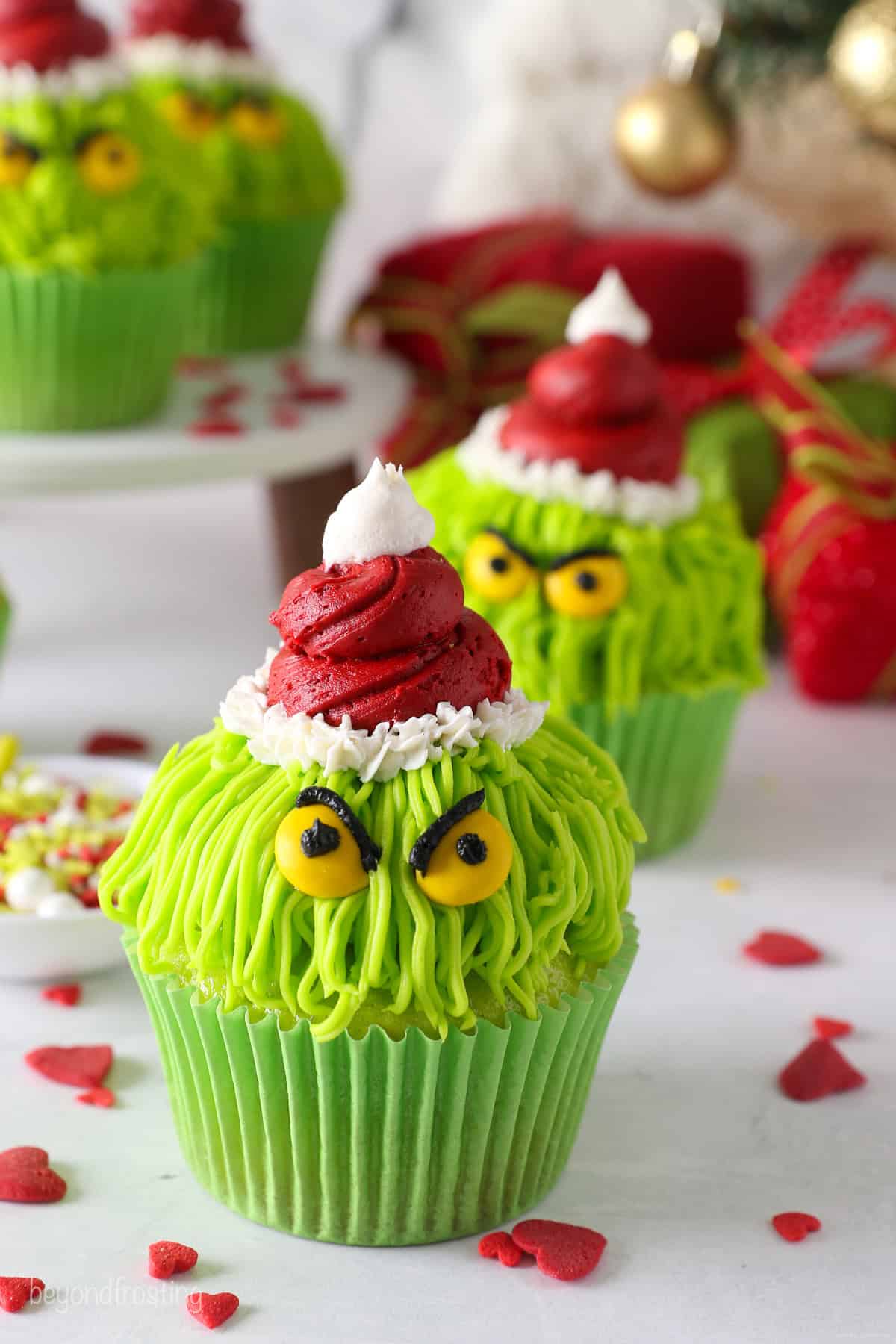 A finished Grinch cupcake decorated with a red frosting Santa hat, yellow M&M eyes, and black frosting details.